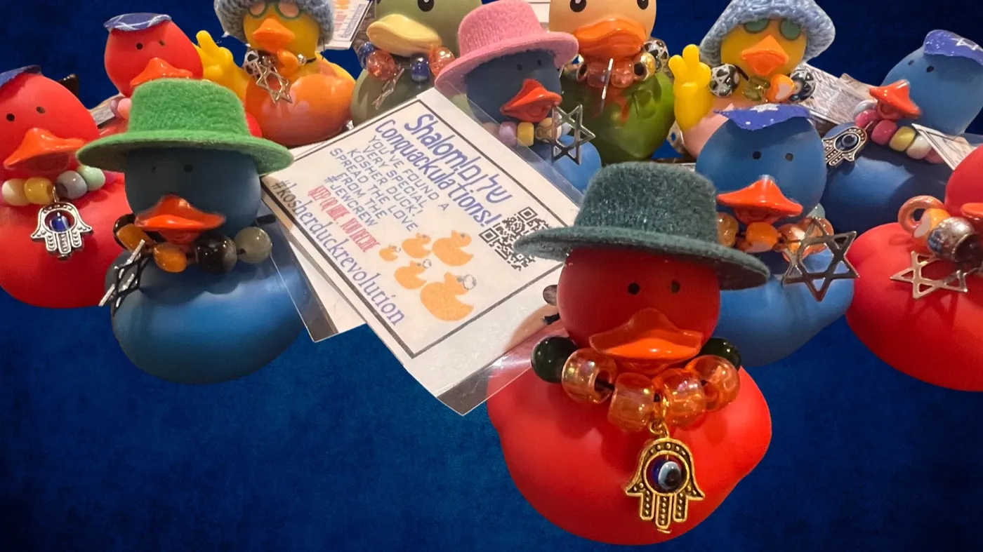 A crowd of kosher ducks in knitted hats and beaded necklaces, with hamsa and Star of David charms, gathered around a tag reading Shalom — ConQuackulations! You've found a very special Kosher Duck